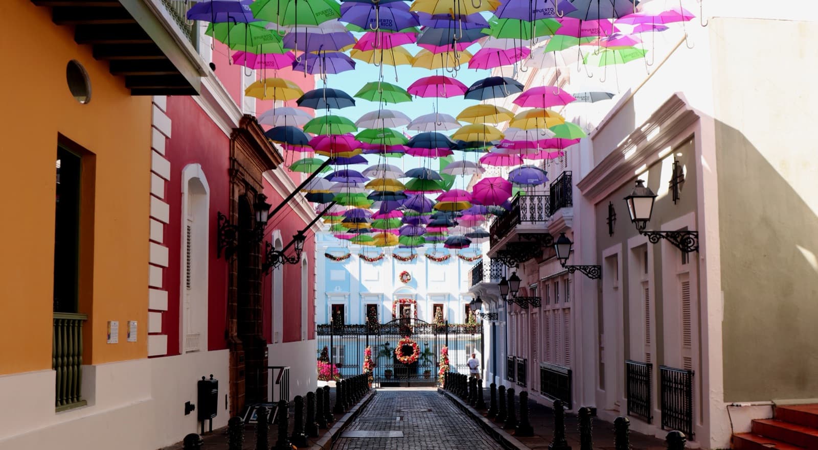 Colorful umbrellas suspended above Calle Fortaleza in Old San Juan, Puerto Rico, with pastel colonial buildings on both sides